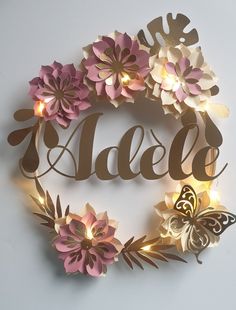 a paper flower wreath with the word adela spelled in gold letters and lighted flowers