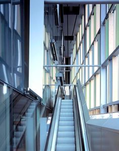 an escalator in a building with glass walls and stairs leading up to the second floor