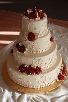 a three tiered wedding cake with red roses on top is sitting on a white tablecloth