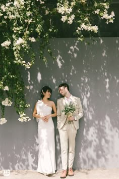 a man and woman standing next to each other in front of a wall with flowers on it