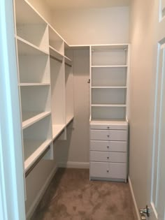 an empty walk in closet with white shelving and drawers on both sides, along with carpeted flooring