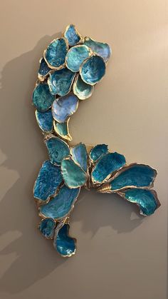 a blue brooch with leaves on it hanging from a wall in front of a beige background