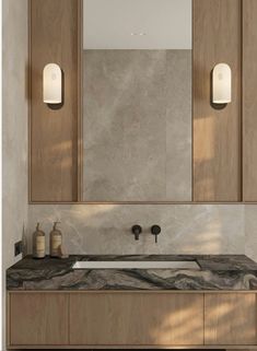 a bathroom vanity with marble counter top and two lights on the wall above it, in front of a mirror