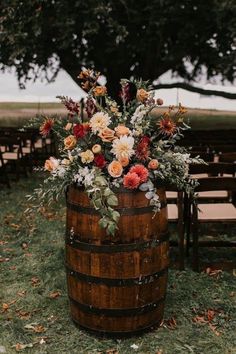 a wooden barrel with flowers and greenery on it sitting in the middle of an outdoor ceremony