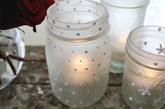 three glass jars with candles in them sitting on a table next to a red rose