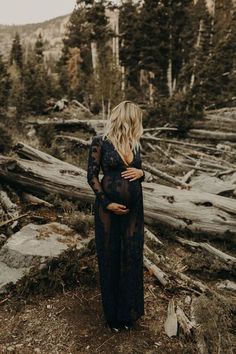 a pregnant woman standing on top of a tree covered hillside in the woods with her back turned to the camera