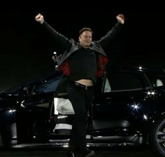 a man standing in front of a black car with his arms up and hands raised