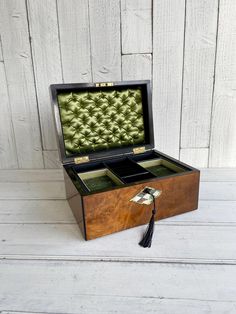 an open wooden box with two compartments and a tassel on the inside, sitting on a white wood floor