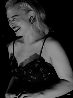 a black and white photo of a woman laughing with her hands on her hips while holding a cell phone