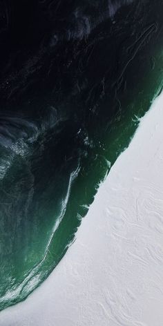 an aerial view of the ocean with waves and snow on the beach, taken from above