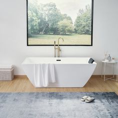 a large white bath tub sitting on top of a wooden floor next to a window