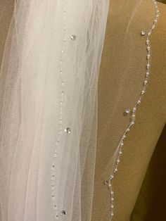 wedding veil with beading and pearls on the bottom, hanging from a mannequin