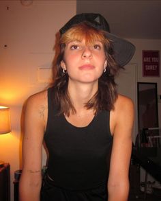 a woman wearing a black top and hat standing in a room with a lamp on the wall