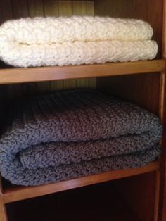 two blankets stacked on top of each other in a wooden shelf next to a wall