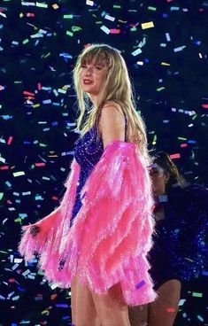 the blond haired woman is dressed in bright pink feathers and blue dress, while confetti falls around her