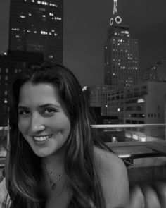 black and white photo of woman smiling in front of cityscape at night time