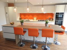 an orange and white kitchen with stools in front of the counter top, lights hanging from the ceiling