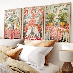 three paintings hang on the wall above a bed with pillows and blankets in front of them