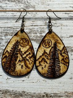 two wooden earrings with pine trees and moon in the sky on them, hanging from a wire