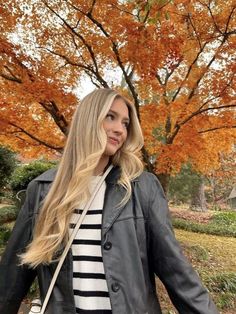 a woman standing in front of a tree wearing a black and white striped shirt, jeans and a leather jacket