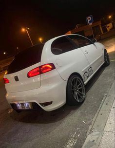 a white car is parked on the side of the road at night with its lights on