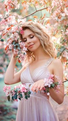 a beautiful young woman in a dress standing under a tree with pink flowers on it