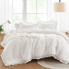 the comforter is white and has ruffled edges on it, along with pillows