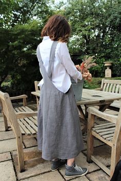 a woman standing in front of a wooden table holding a bucket filled with leaves and flowers