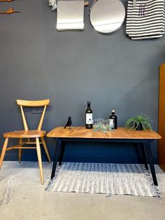 a wooden table sitting in front of a gray wall next to a chair and mirror