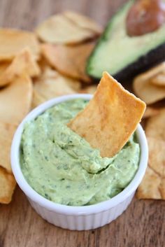 a white bowl filled with guacamole and chips on top of a wooden table