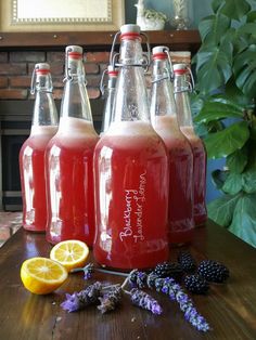 three glass bottles filled with liquid sitting on top of a table next to lemons and blackberries