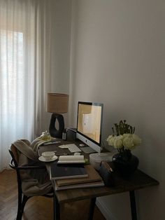 a desk with a computer on top of it next to a lamp and vase filled with flowers