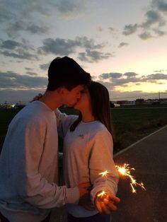 two people standing next to each other with sparklers in their hands and the sun setting behind them