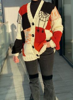 a woman standing in front of a building wearing boots and a sweater with spider webs on it