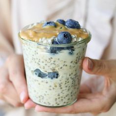 a person holding a glass with some food in it and blueberries on the top