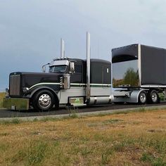 a large semi truck is parked on the side of the road in front of an empty field