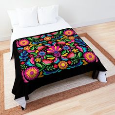 a bed covered in a colorful blanket on top of a wooden floor next to a white wall