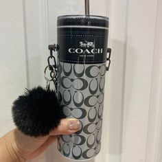 a hand holding a black pom - pom in front of a coach bottle