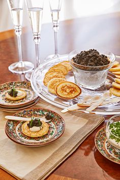 a wooden table topped with plates and bowls filled with food next to wine glasses on top of each other