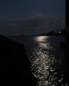 the moon is shining over the water at night