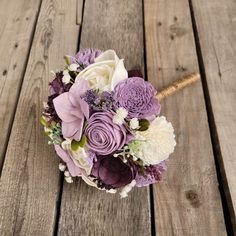 a bridal bouquet with purple and white flowers on a wooden table, ready to be used as a bride's bouquet