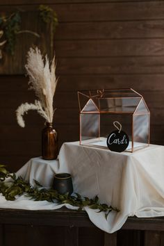 a table topped with a small glass box filled with greenery and a chalkboard sign