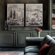 two black and white paintings on the wall above a couch in front of a bookshelf