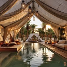 an indoor swimming pool surrounded by white drapes and lit candles with palm trees in the background