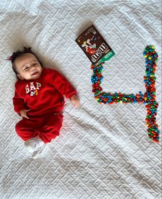 a baby laying on top of a bed next to a candy beaded letter h