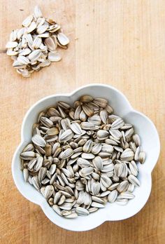 a white bowl filled with sunflower seeds on top of a wooden table