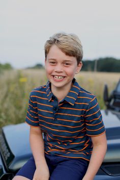 a young boy sitting on the hood of a car