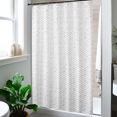 a white shower curtain in a bathroom next to a toilet and sink with a potted plant