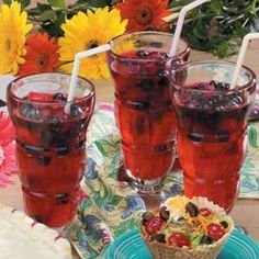 three glasses filled with red liquid sitting on top of a blue plate next to flowers