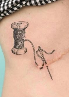 a tattoo on the side of a woman's stomach shows a spool of thread and a needle